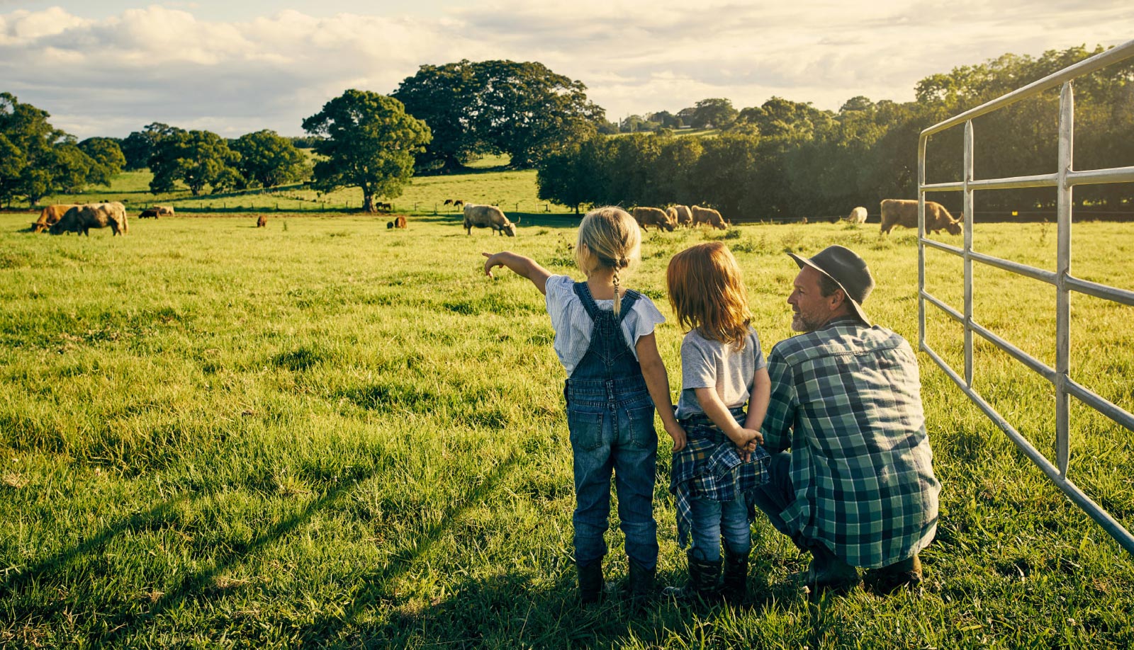 Family of a father and his two cute daughters staring out at a large farm with cows grazing